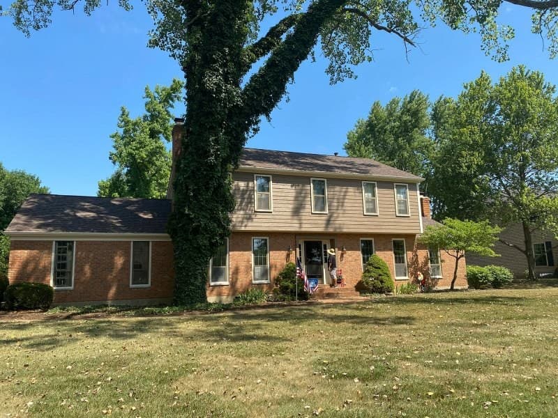 Two-story brick and siding house behind large tree